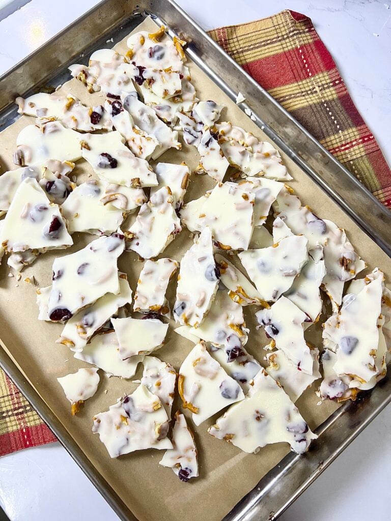 White Chocolate Pretzel Bark Christmas candy cooling on a baking sheet, made with pretzels, cranberries, and chopped nuts