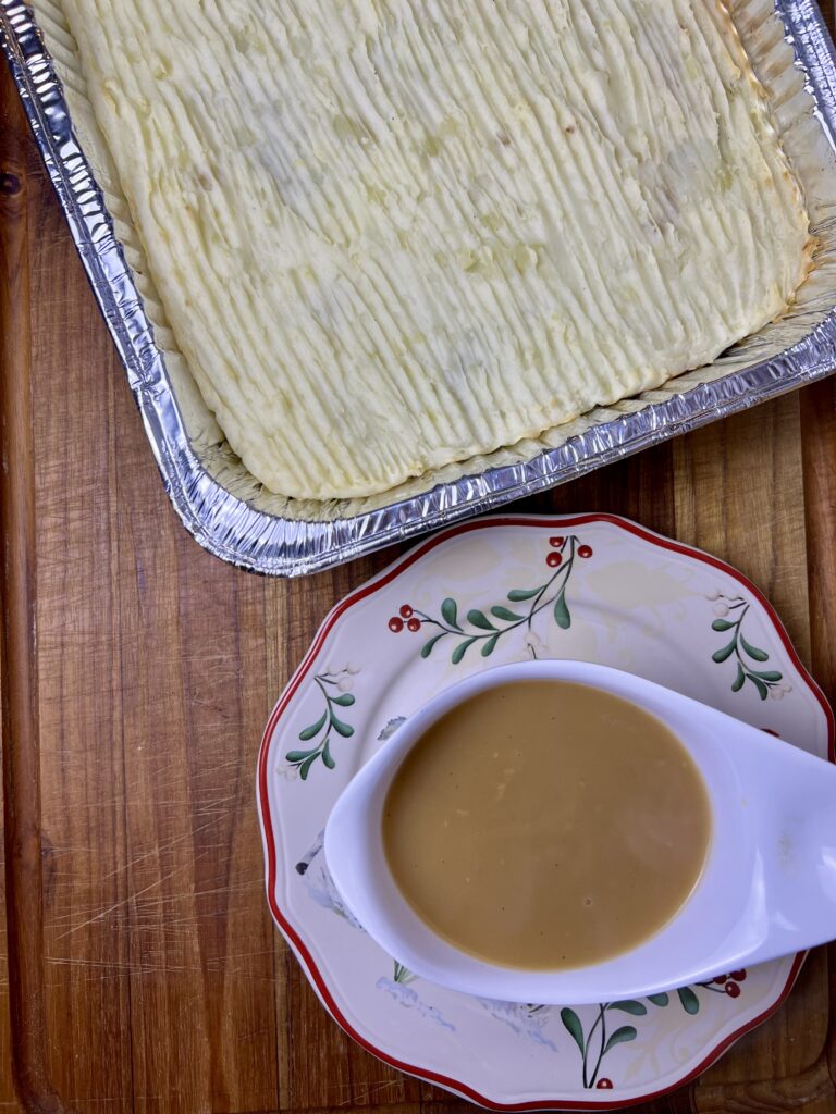 Thanksgiving casserole with leftovers in a 9x13 dish, topped with mashed potatoes and served with homemade turkey gravy