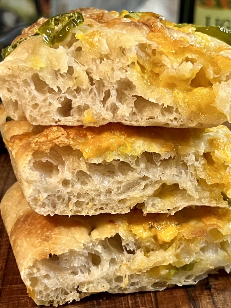 Stacked slices of jalapeño cheddar sourdough focaccia showing an open airy crumb, gooey melted cheese, and tender sourdough texture.