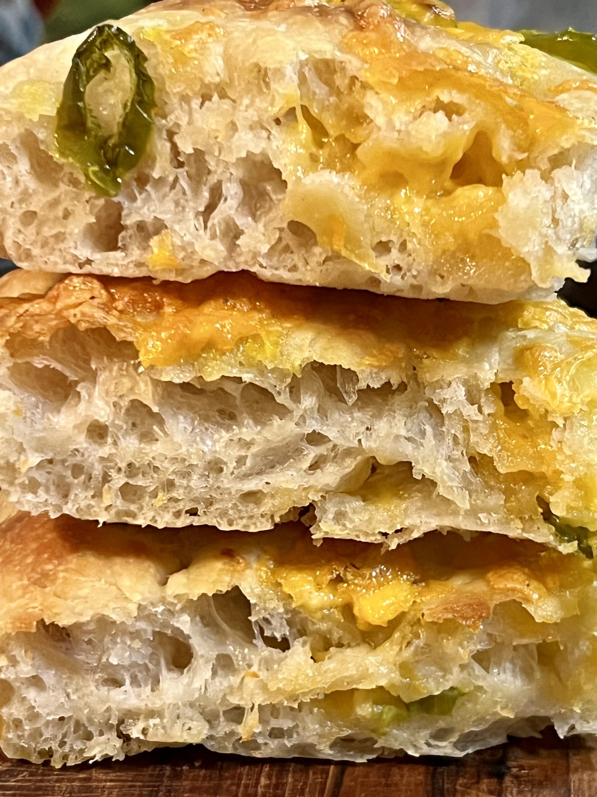 Close-up of sliced sourdough jalapeño cheddar focaccia showing an airy open crumb, melted sharp cheddar cheese, and tender jalapeño pieces baked into golden no-knead sourdough bread.