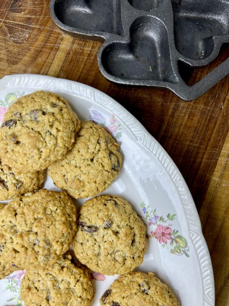 Homemade oatmeal raisin cookies arranged on a vintage floral plate, golden brown and soft, photographed on a wooden countertop with baking pan nearby