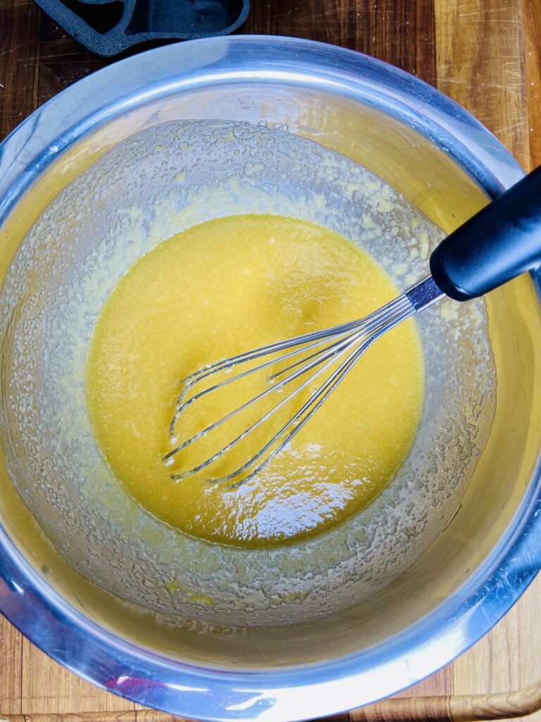 Melted butter and sugar mixture whisked together in a stainless steel mixing bowl for oatmeal raisin cookies