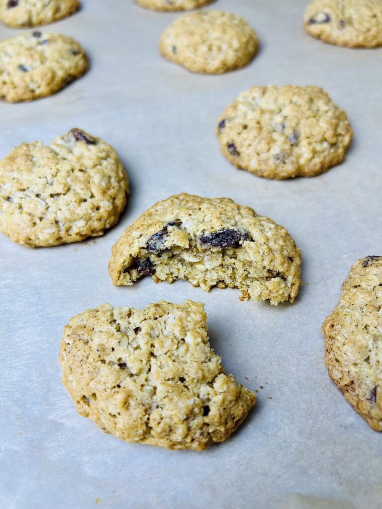 Freshly baked oatmeal raisin cookies on baking sheet with one cookie broken open to show soft chewy interior