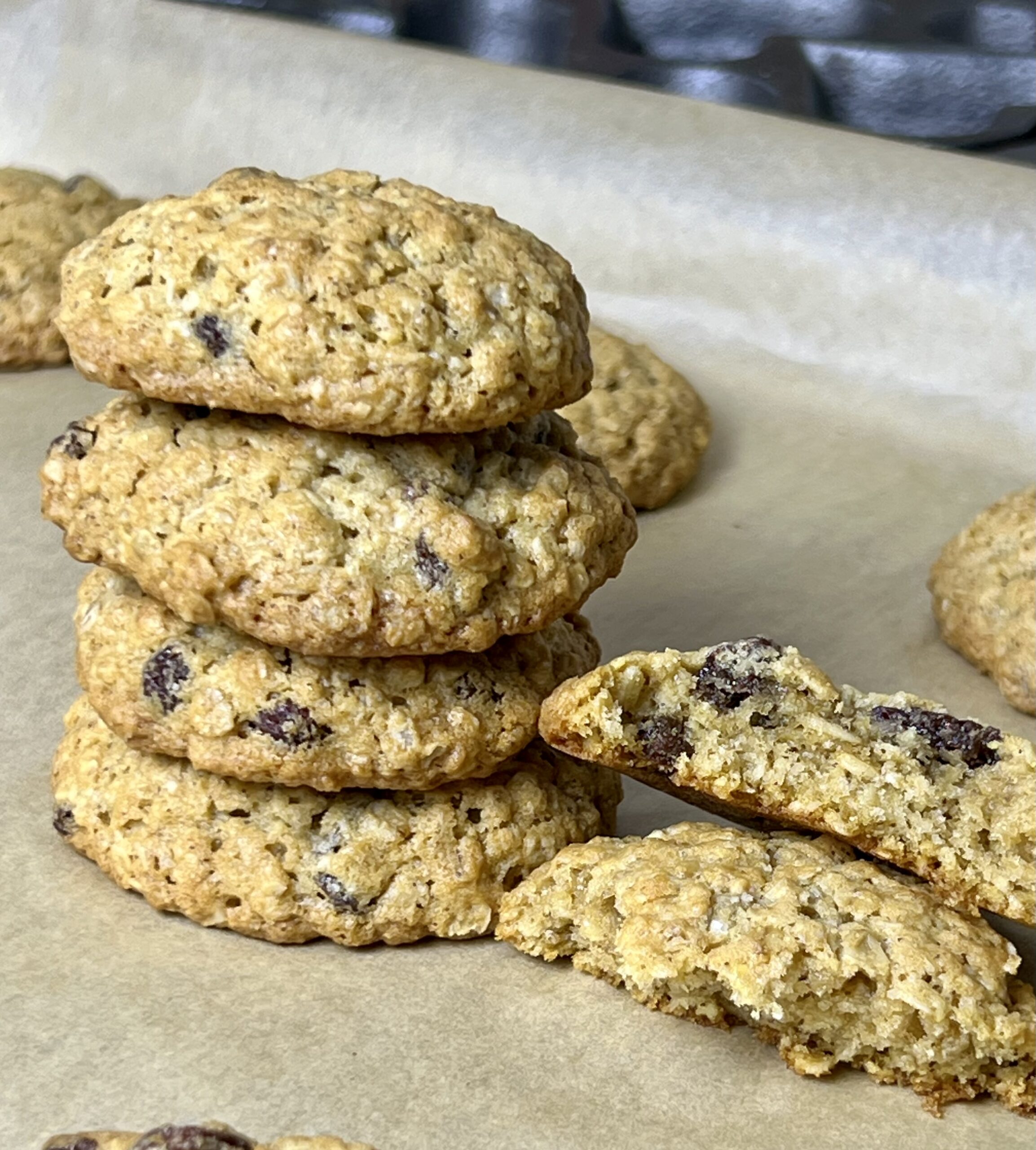 Stack of homemade oatmeal raisin cookies on parchment paper, with one cookie broken open to show a soft, chewy center filled with oats and raisins. Classic old-fashioned oatmeal raisin cookies baked from Grandma’s traditional recipe, golden brown with crisp edges and tender texture.