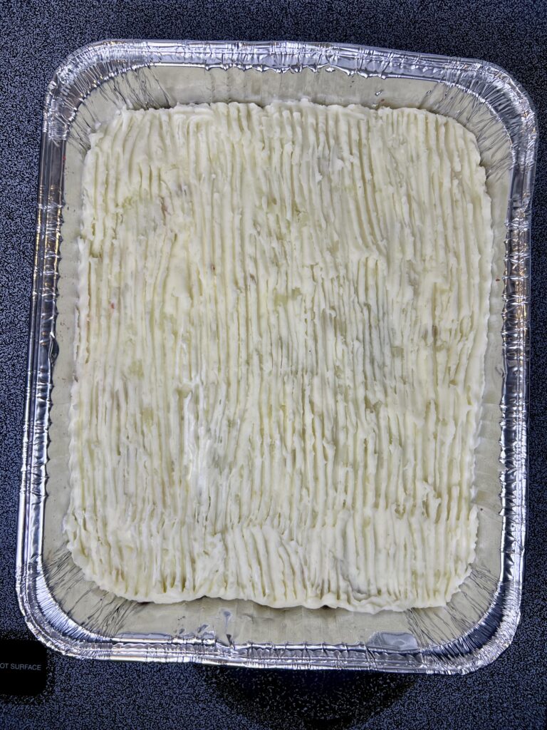 Thanksgiving leftover casserole baked in a foil pan, featuring mashed potato topping over layered turkey, stuffing, and cranberry sauce