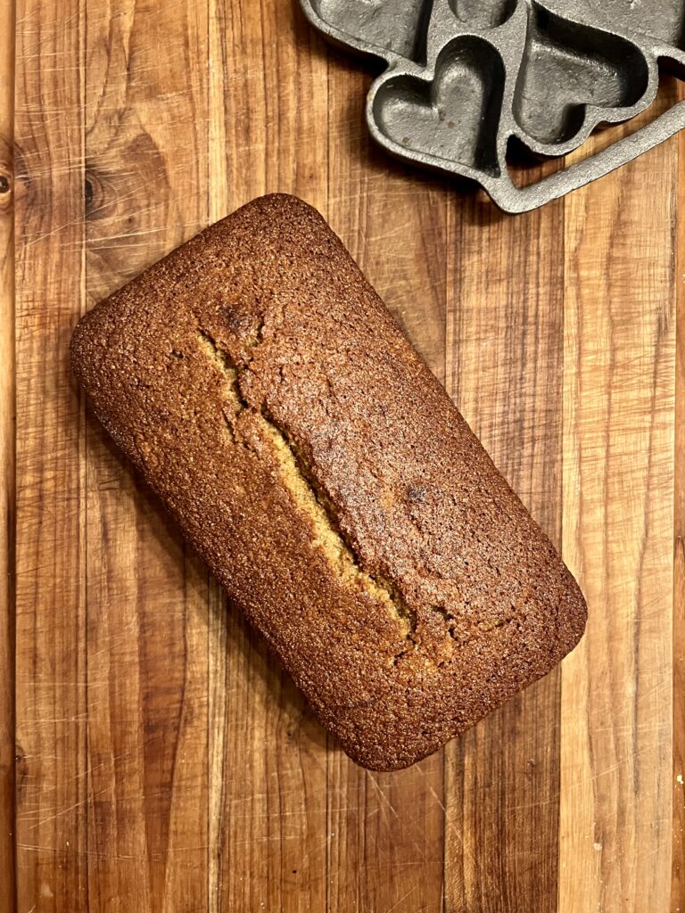 Baked fresh milled banana bread loaf cooling on a wooden cutting board, made with freshly milled soft white wheat flour