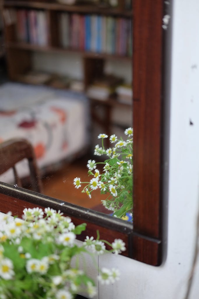 Chamomile flowers reflected in a mirror, capturing a cozy room with shelves and a bed.
