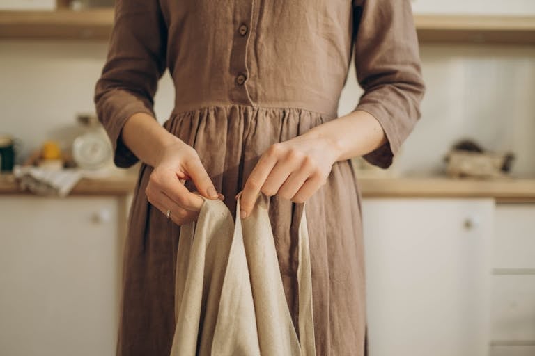 Close-up of a woman adjusting her apron in a rustic kitchen setting, wearing a brown dress.