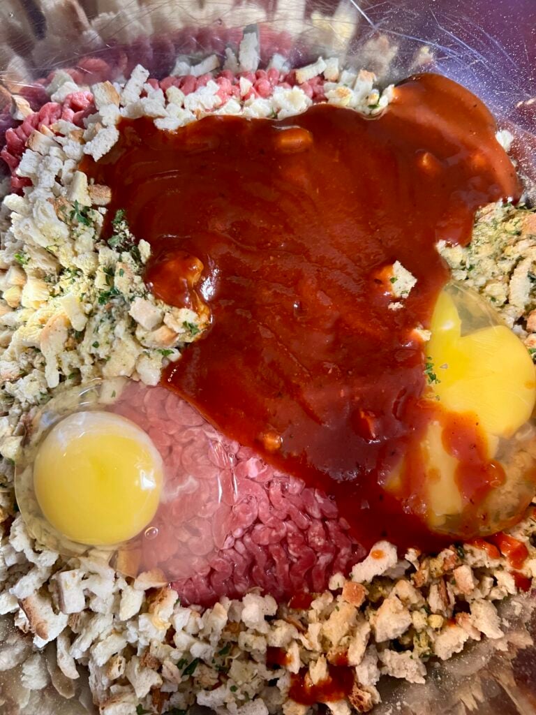 Ground beef, stuffing mix, eggs, water, and BBQ sauce combined in a mixing bowl, showing ingredients used for an easy meatloaf recipe with few ingredients.