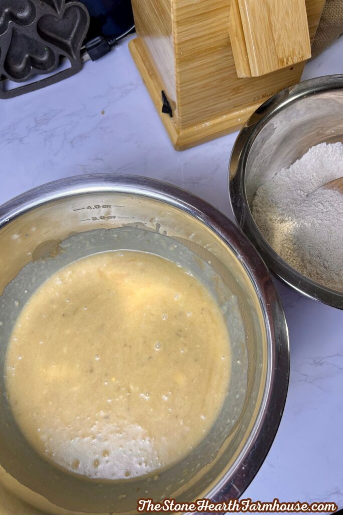 Mashed banana bread batter with wet ingredients mixed together in a stainless steel bowl