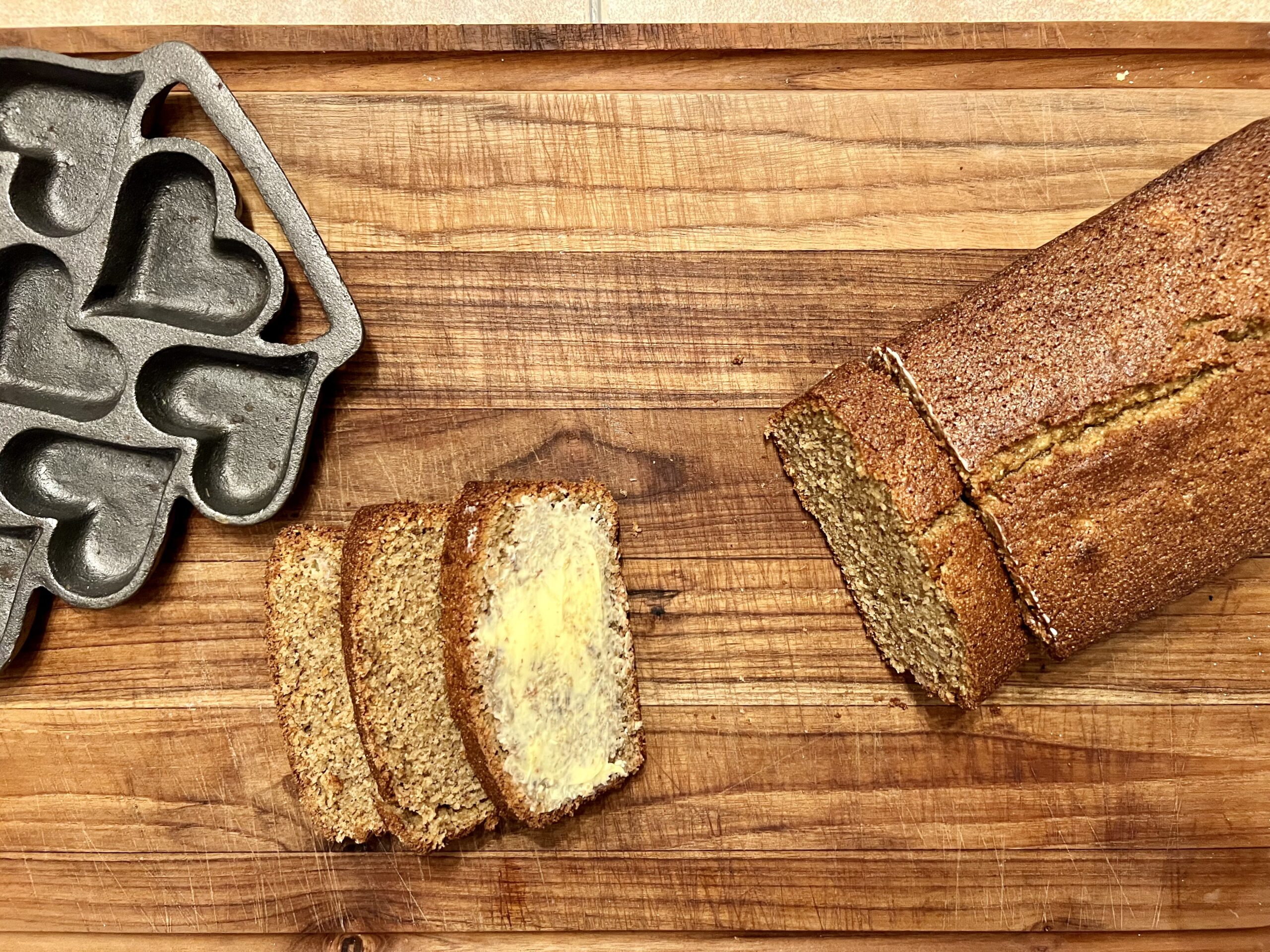 Slices of fresh milled banana bread spread with butter on a wood cutting board, showing moist texture made with freshly milled flour