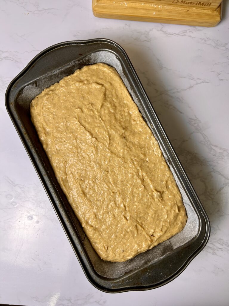 Fresh milled banana bread batter spread into a loaf pan before baking, made with soft white wheat flour and ripe bananas