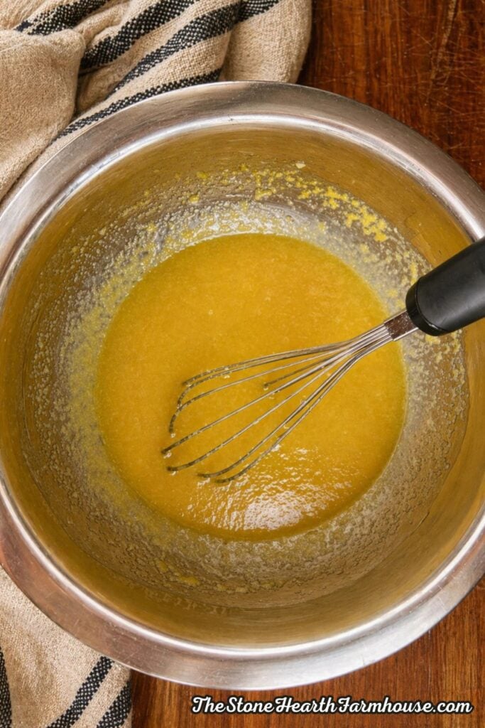 Melted butter and sugar mixture whisked together in a stainless steel mixing bowl for oatmeal raisin cookies