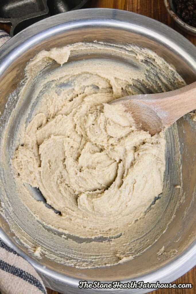 Creamed butter and sugar mixture in a mixing bowl with wooden spoon, smooth and pale before adding oats