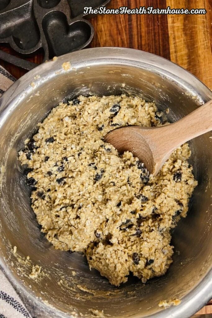 Oatmeal raisin cookie dough mixed with rolled oats and raisins in a stainless steel bowl with wooden spoon