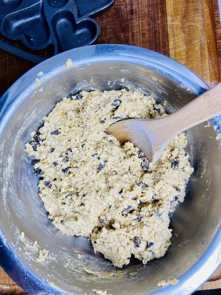 Oatmeal raisin cookie dough mixed with rolled oats and raisins in a stainless steel bowl with wooden spoon