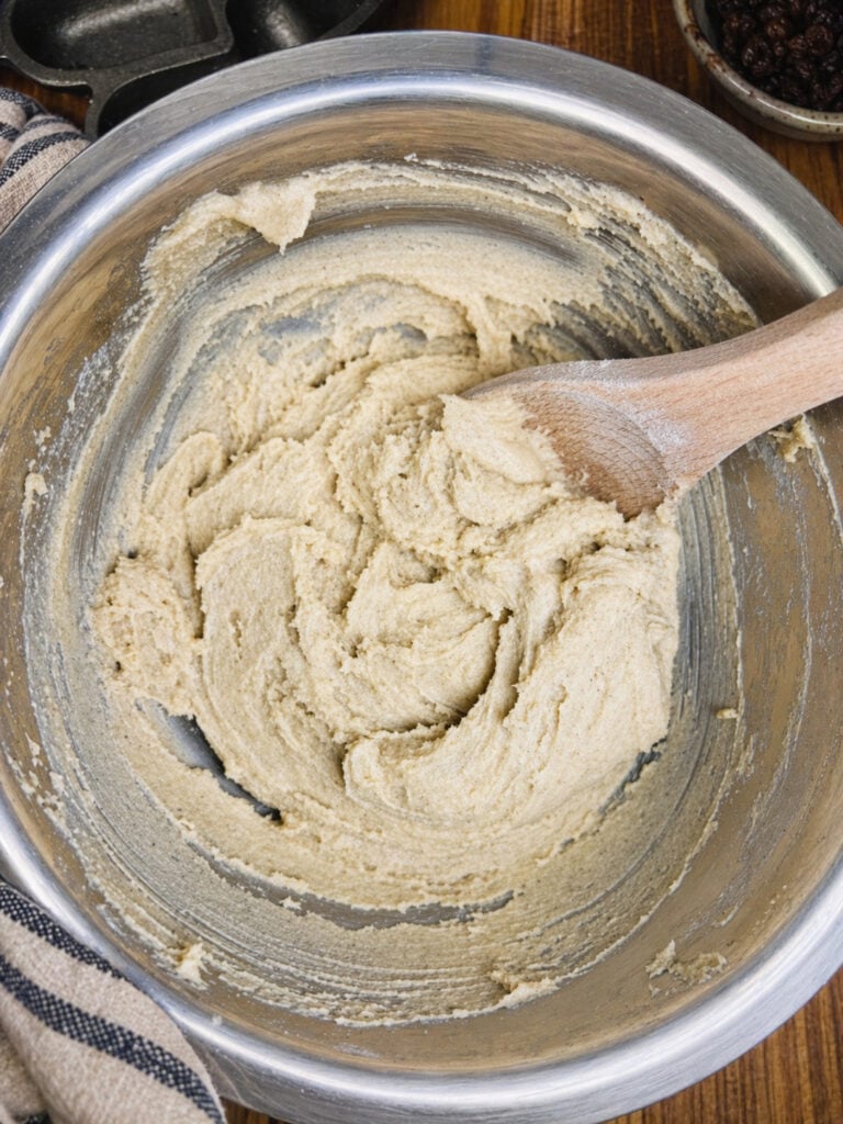 Creamed butter and sugar mixture in a mixing bowl with wooden spoon, smooth and pale before adding oats