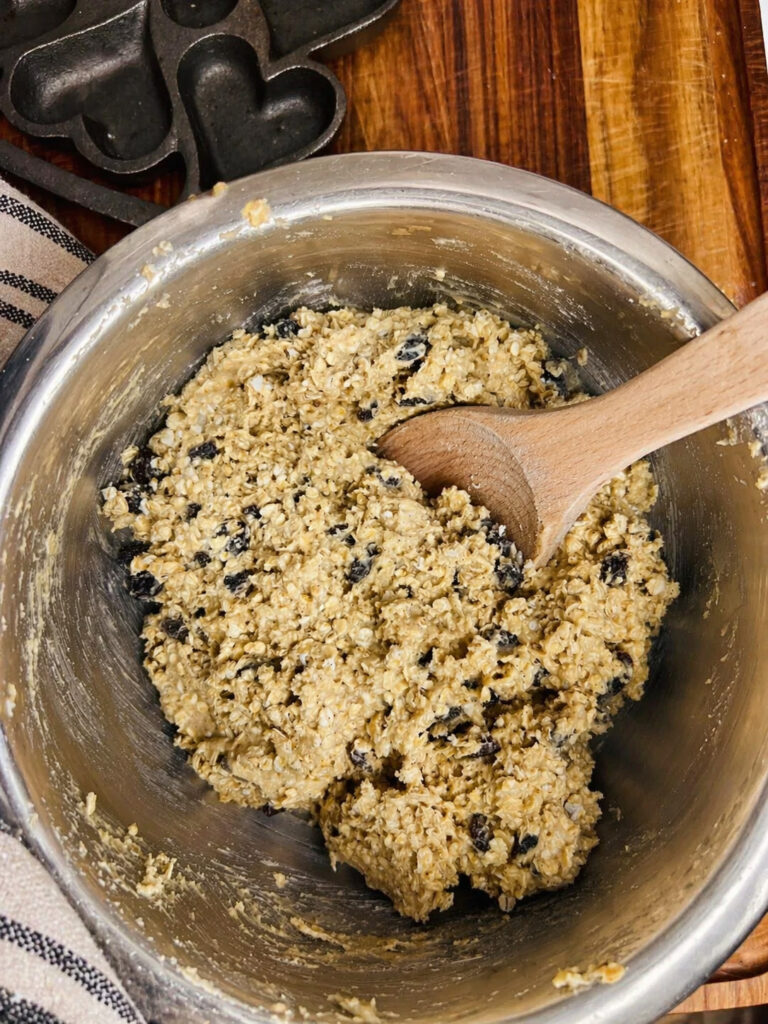 Oatmeal raisin cookie dough mixed with rolled oats and raisins in a stainless steel bowl with wooden spoon