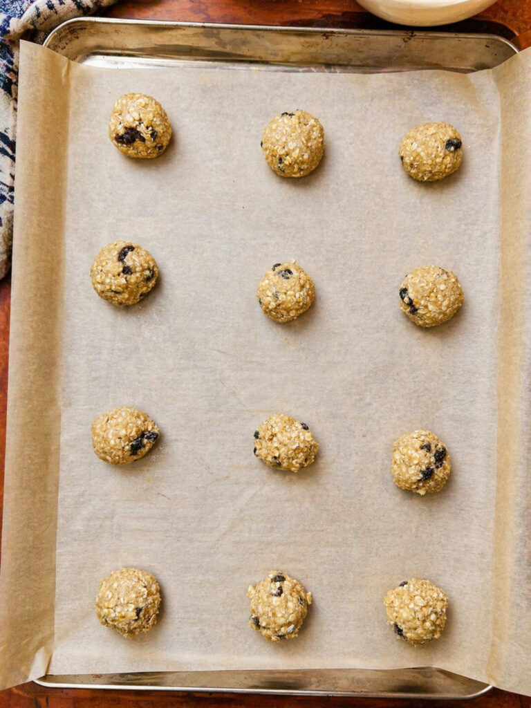 Oatmeal raisin cookie dough scooped into round balls and spaced evenly on a parchment lined baking sheet