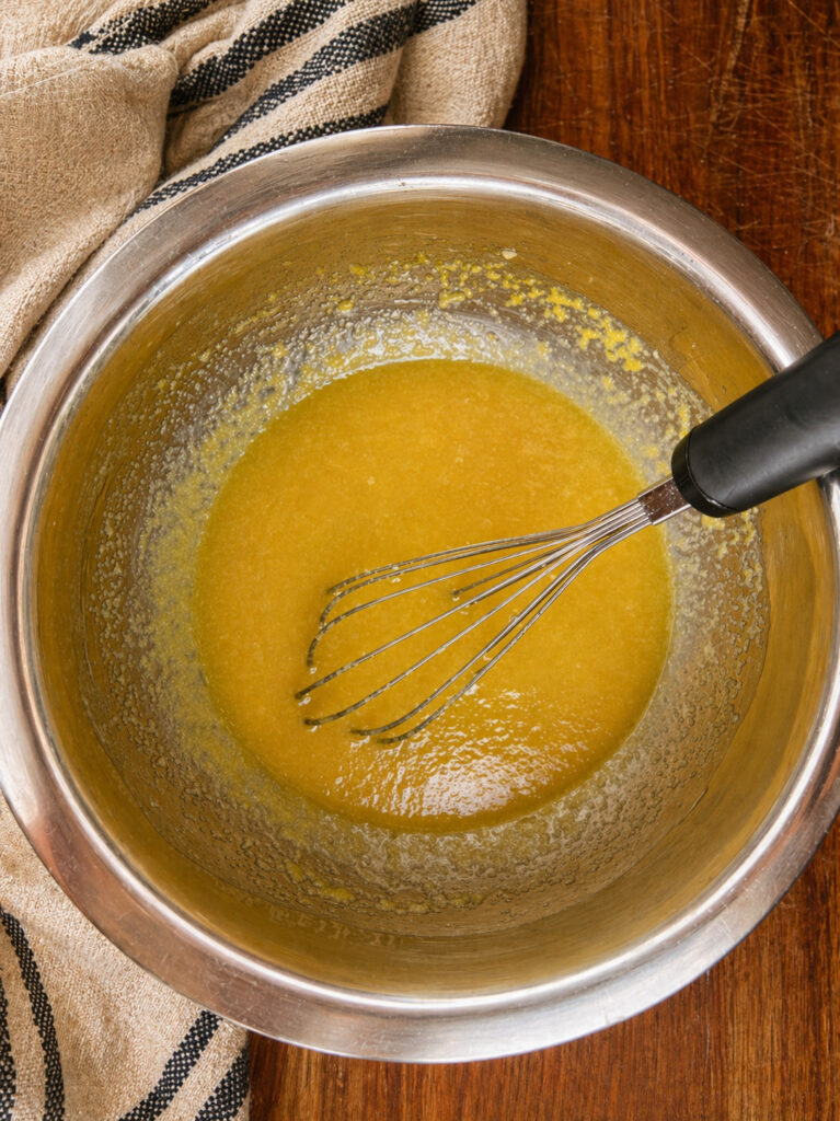 Melted butter and sugar mixture whisked together in a stainless steel mixing bowl for oatmeal raisin cookies