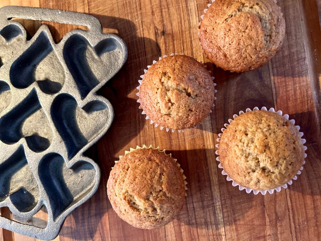 sourdough banana muffins on a wooden cutting board with a heart cast iron tray next to them. 