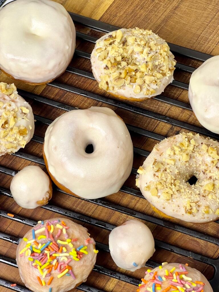close up of sourdough donuts on a cooling rack, freshly coated with glaze, nuts and sprinkles.