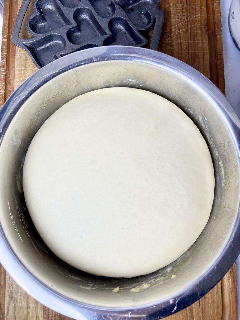 sourdough donut dough fermented and risen almost to the brim of a stainless steel bowl. It is ready to be rolled put and cut into donuts.
