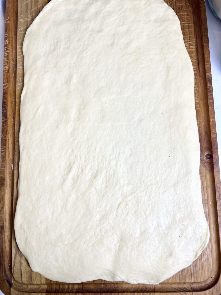 Dough is rolled out on a wooden cutting board and ready to be shaped into donuts.