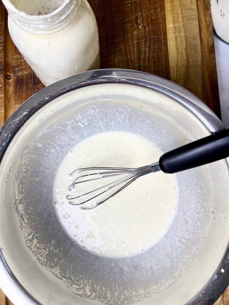 The wet ingredients for the donuts dough in a stainless steel bowl with a whisk.