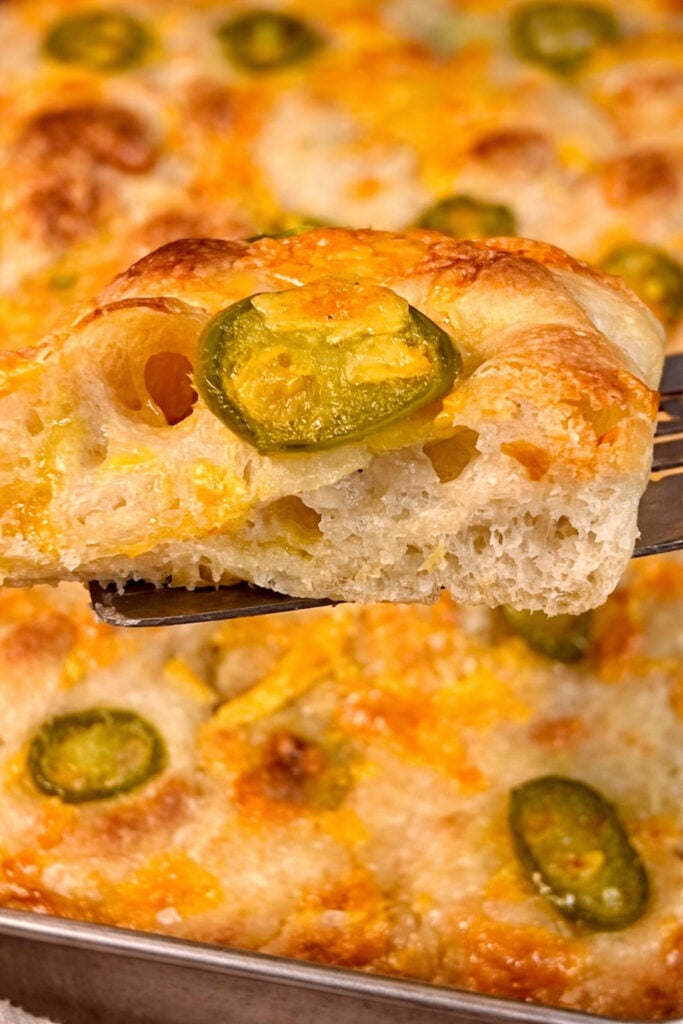 Close-up of a slice of jalapeño cheddar sourdough focaccia lifted from the pan, highlighting soft interior crumb and melted cheddar.