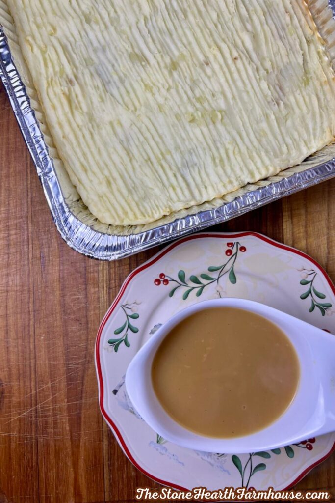 Thanksgiving casserole topped with mashed potatoes served with a bowl of gravy on a holiday table.