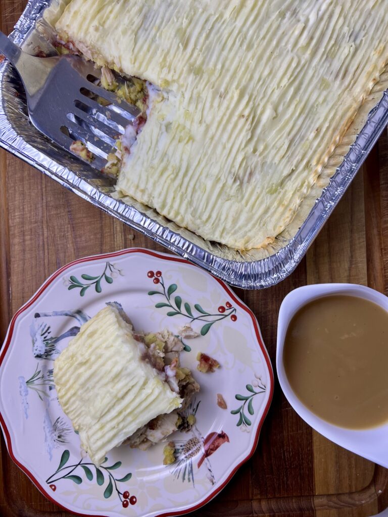 Thanksgiving leftover lasagna served with gravy, made as a layered thanksgiving casserole with turkey, stuffing, cranberry sauce, and mashed potatoes