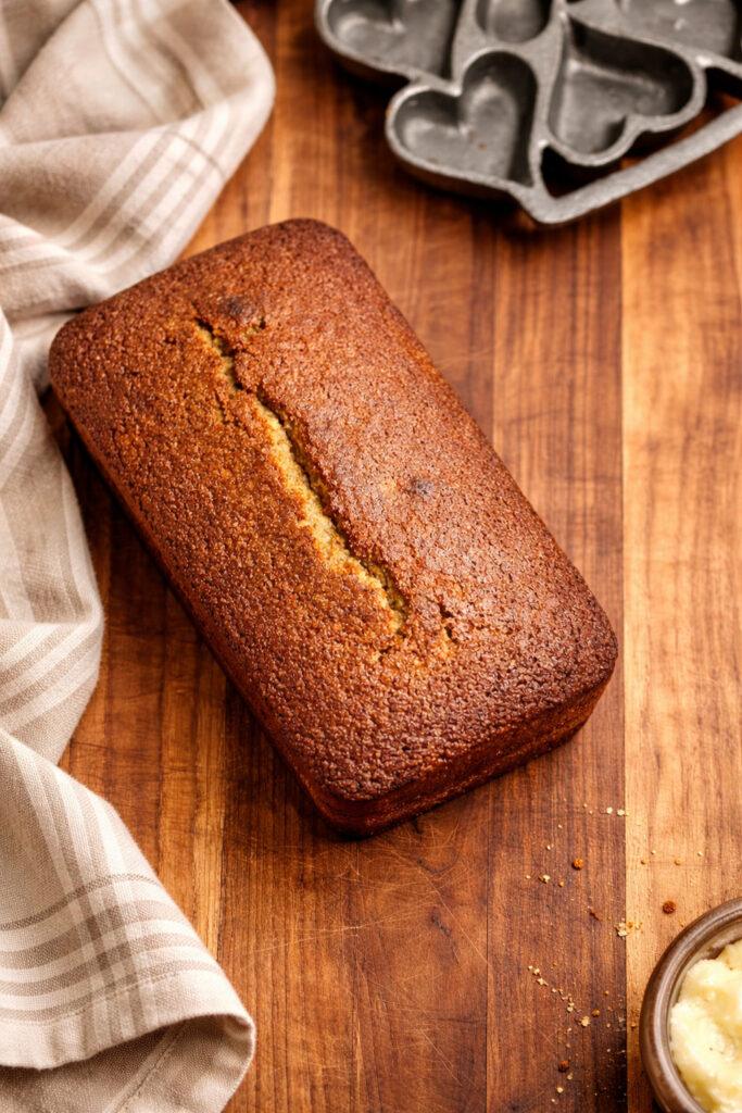 Baked fresh milled banana bread loaf cooling on a wooden cutting board, made with freshly milled soft white wheat flour