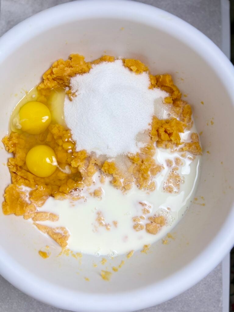 Canned yams combined with eggs, sugar, and milk in mixing bowl for Sweet Potato Casserole with Canned Yams before stirring together.