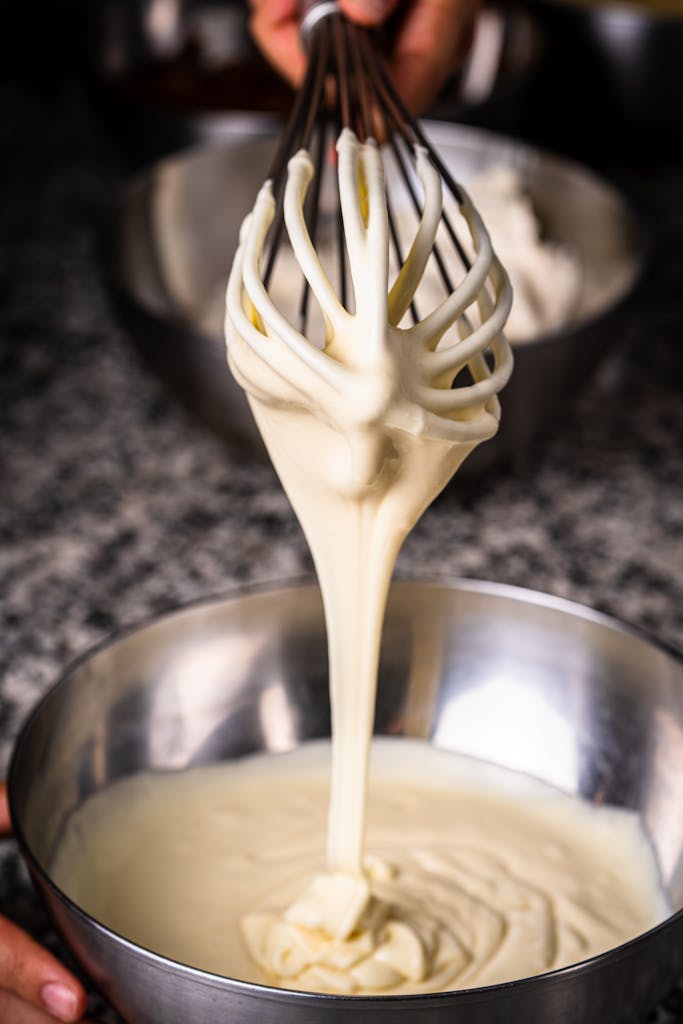 Vanilla icing for ricotta cookies being whisked in a metal bowl, ready to spread over warm cookies.