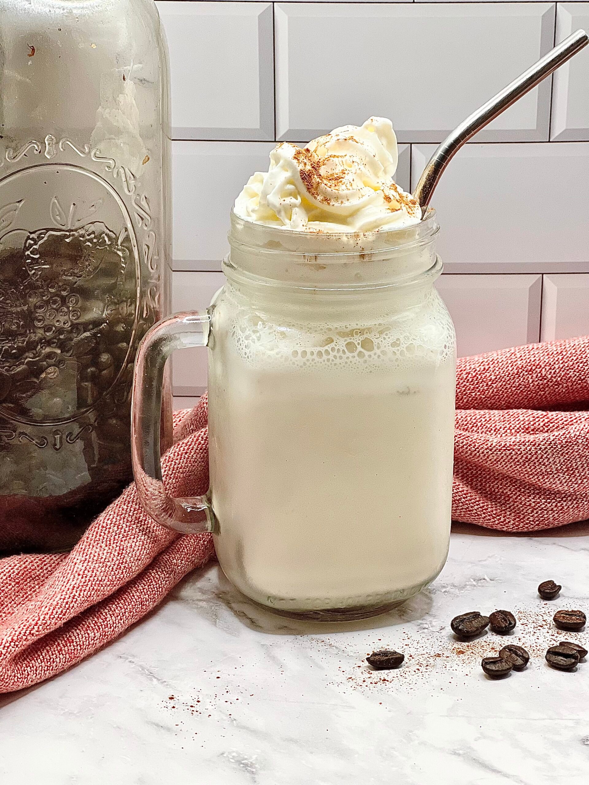 Homemade frosted coffee topped with whipped cream and cinnamon in a mason jar, creamy vintage iced coffee drink made with coffee syrup and vanilla ice cream.