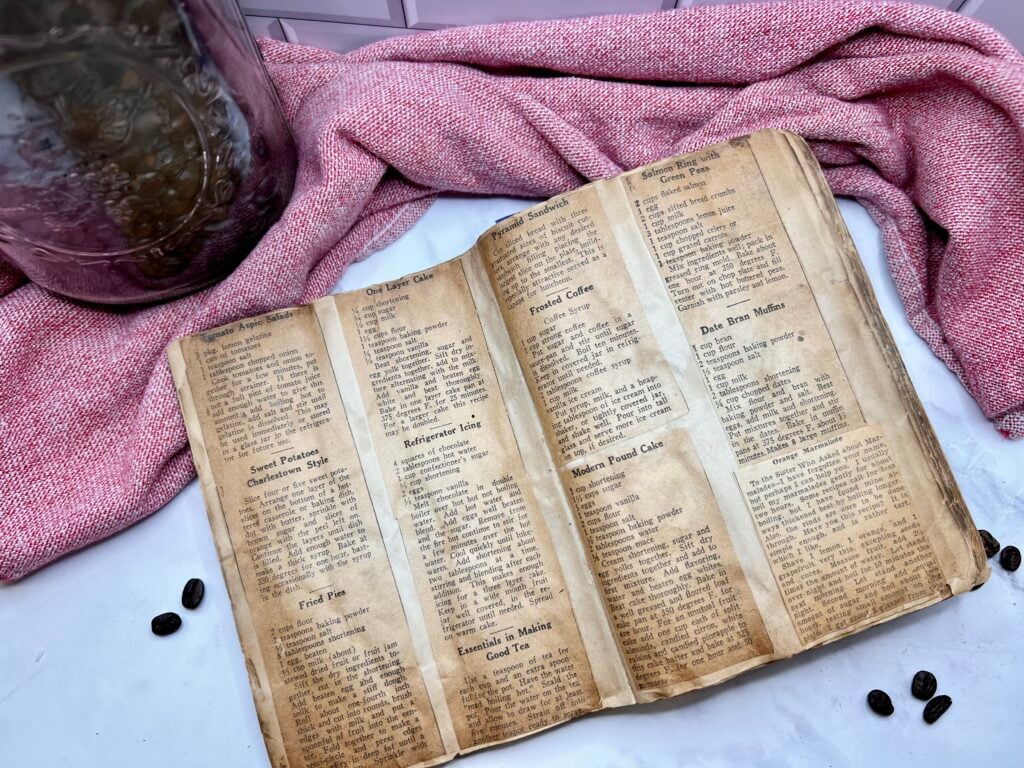 Open antique cookbook displaying a vintage recipe styled with coffee beans and rustic kitchen decor for an old-fashioned homemade drink.