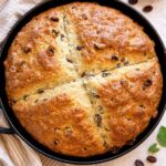 Round homemade Irish soda bread made with sourdough discard and raisins, baked until golden brown in a cast iron skillet.