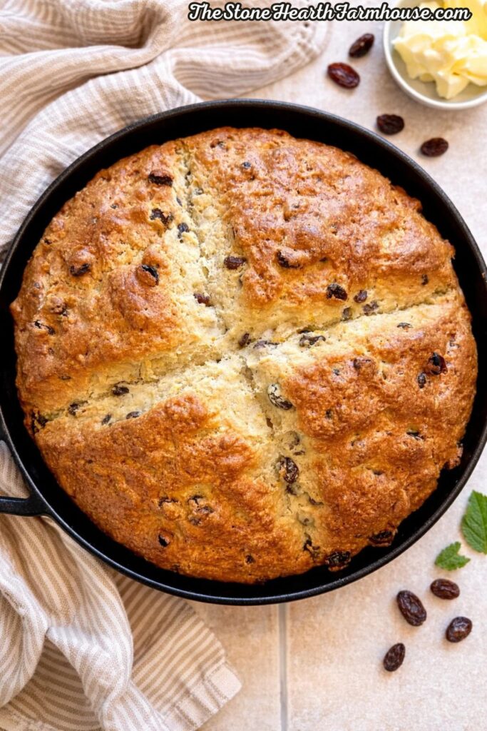 golden brown sourdough Irish soda bread in cast iron skillet with raisins and rustic kitchen towel