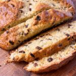 Sliced homemade sourdough Irish soda bread with raisins on a wooden cutting board, showing the golden crust and tender crumb.
