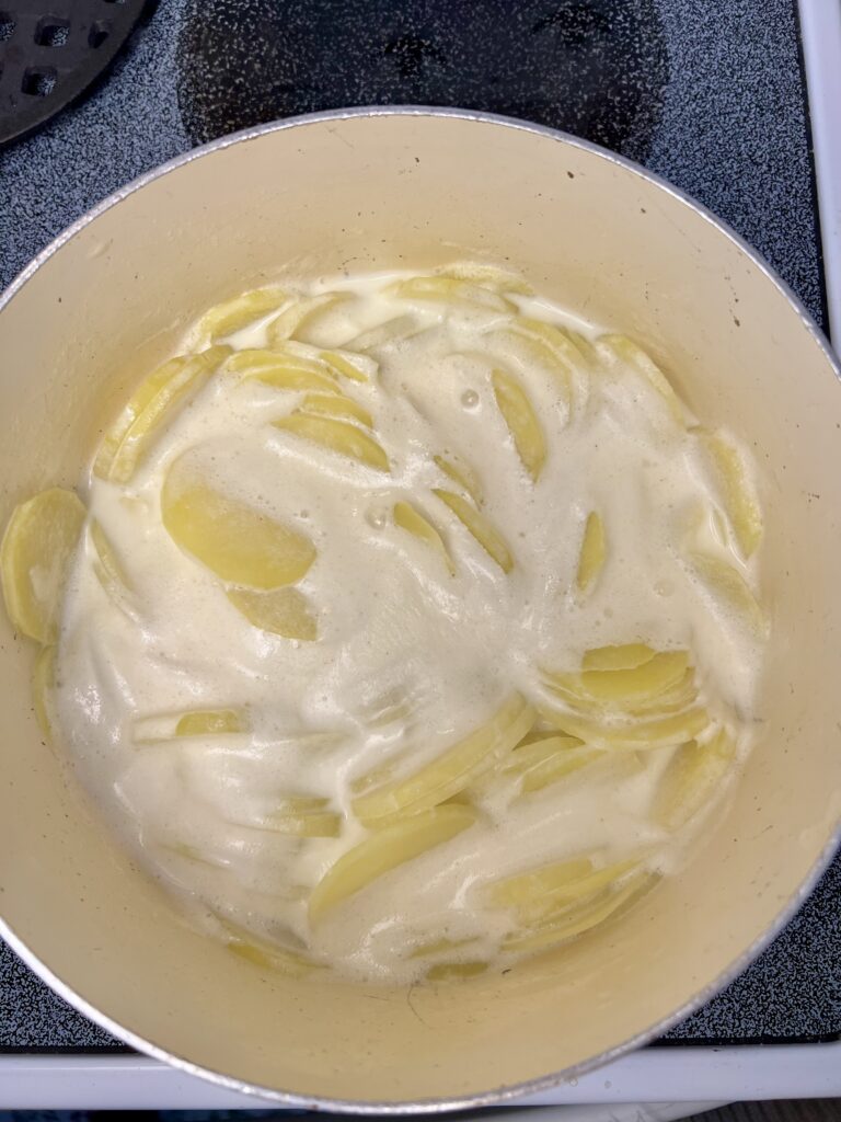 Yukon gold potato slices simmering in half and half on stovetop for homemade cheddar potato gratin.