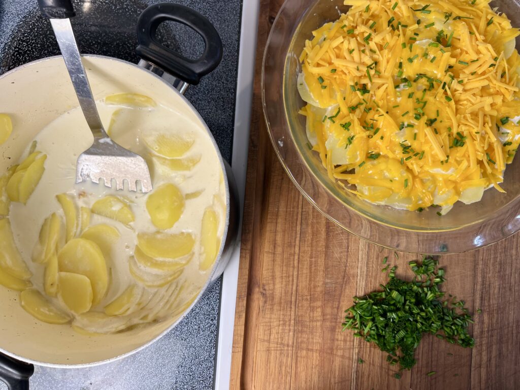 Layering thinly sliced potatoes with shredded sharp cheddar and fresh chives in baking dish for cheddar potato gratin.