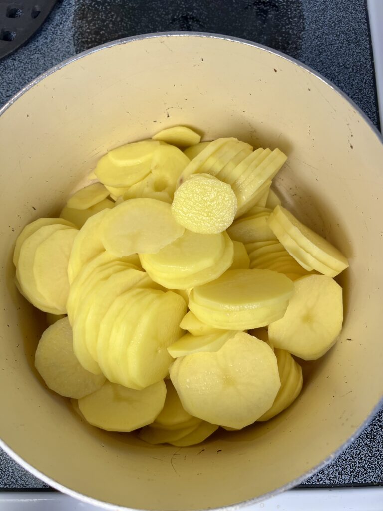 Thinly sliced Yukon gold potatoes in a pot, prepped for creamy cheddar potato gratin recipe.