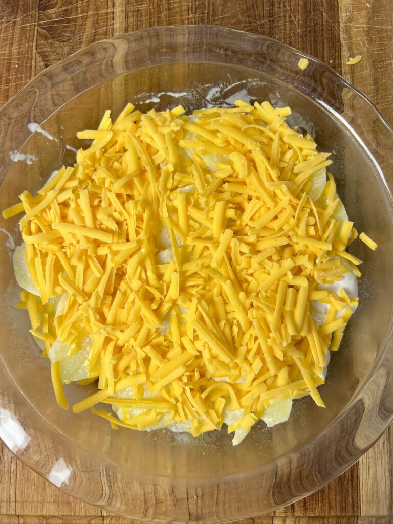 Unbaked cheddar potato gratin layered with Yukon gold potatoes and shredded cheddar cheese in glass casserole dish.