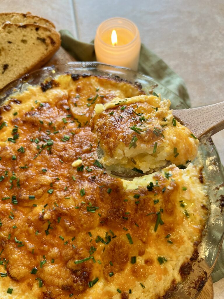 Spoon lifting a creamy serving of cheddar potato gratin with melted sharp cheddar and tender Yukon gold potatoes, baked until golden and bubbly.