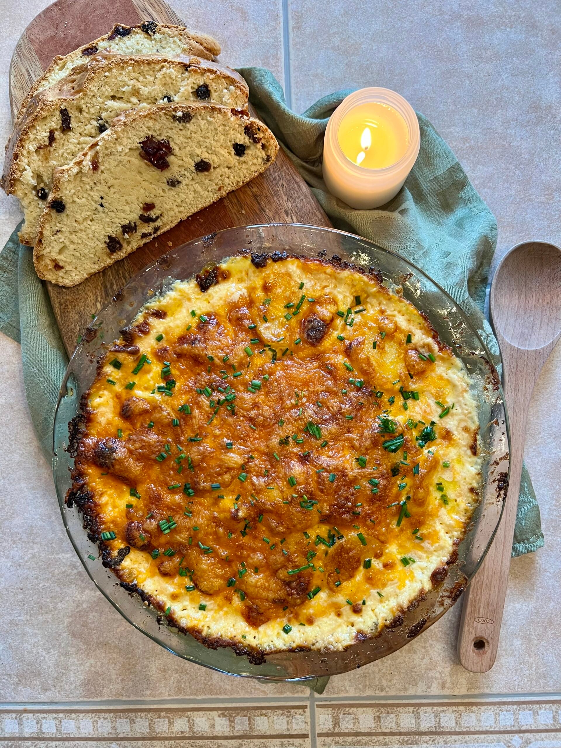 Overhead view of cheesy cheddar potato gratin topped with fresh chives in a glass baking dish, classic baked potato gratin recipe for holidays.