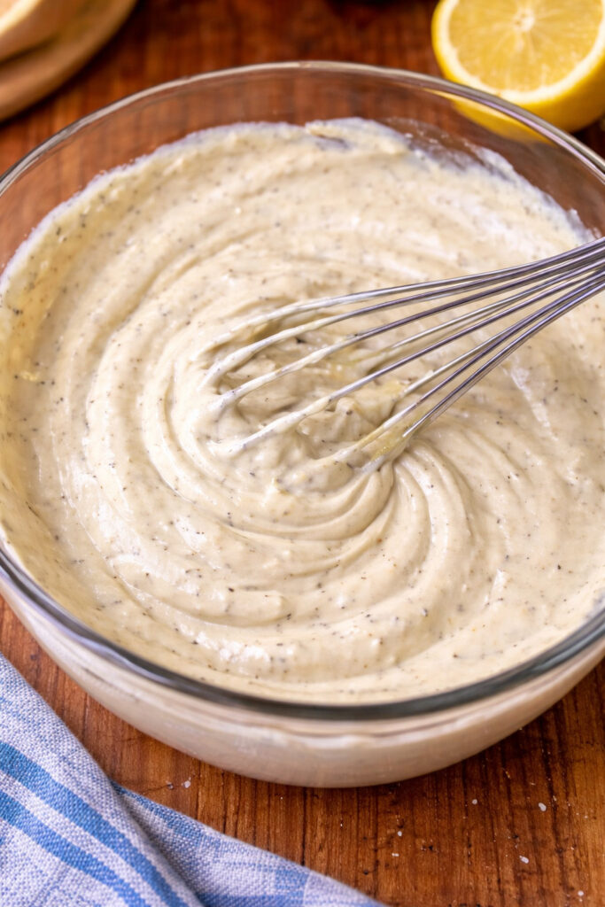 Creamy dressing being whisked in a glass bowl with lemon juice and spices for a chicken salad recipe for a crowd