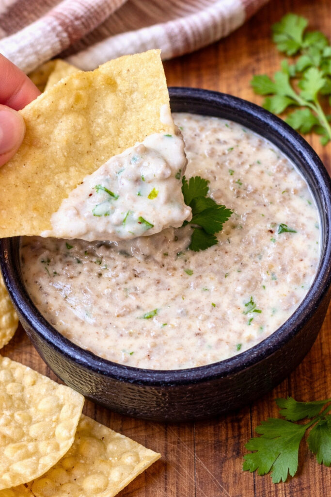 Creamy queso dip with ground beef topped with fresh cilantro served with tortilla chips for dipping.