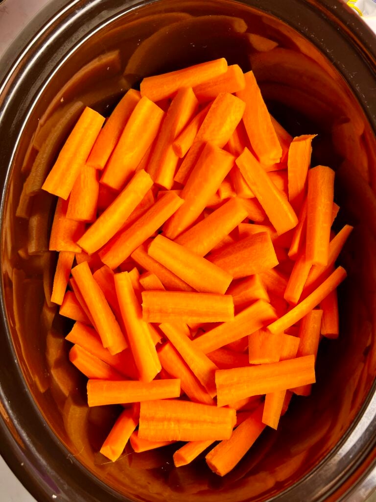 Raw carrot sticks in crock pot prepared for slow cooker glazed carrots recipe.