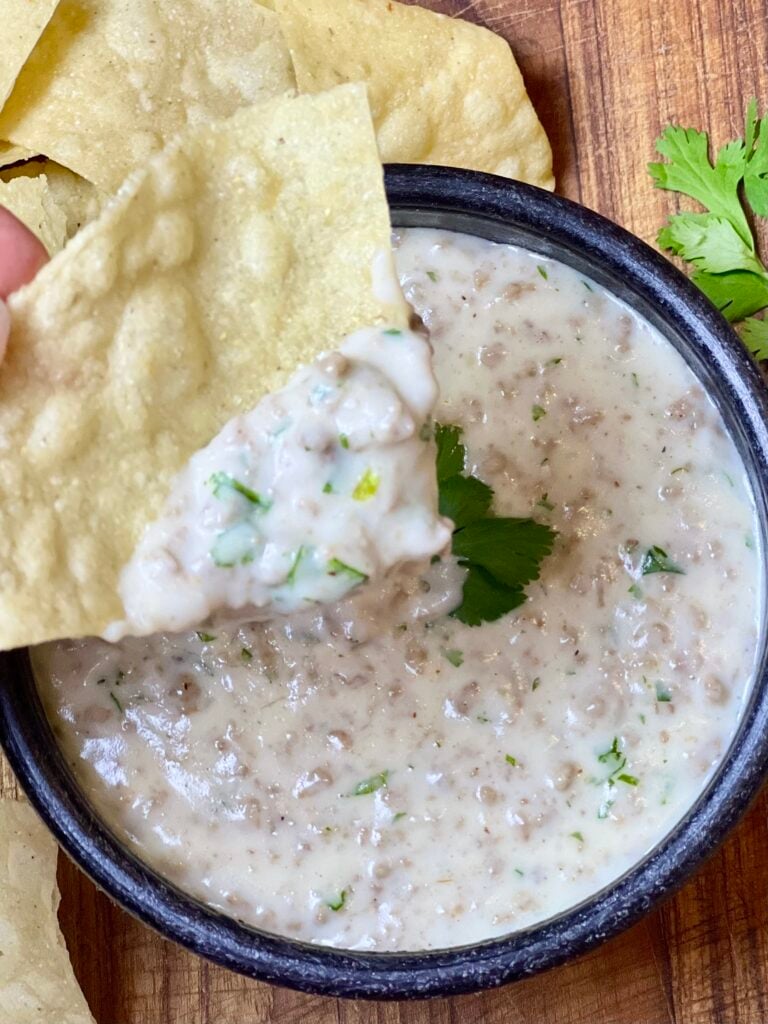 Creamy queso dip with ground beef topped with fresh cilantro served with tortilla chips for dipping.